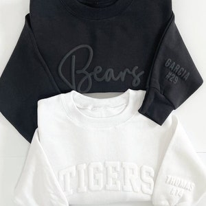 Peut inclure: Deux sweat-shirts col rond, un noir et un blanc, sont pr&eacute;sent&eacute;s. Le sweat-shirt noir porte l'inscription "Bears" en &eacute;criture cursive et "GARCIA #29" sur la manche. Le sweat-shirt blanc affiche "TIGERS" et "THOMAS #14" sur la manche. La marque "little looks" est en bas.