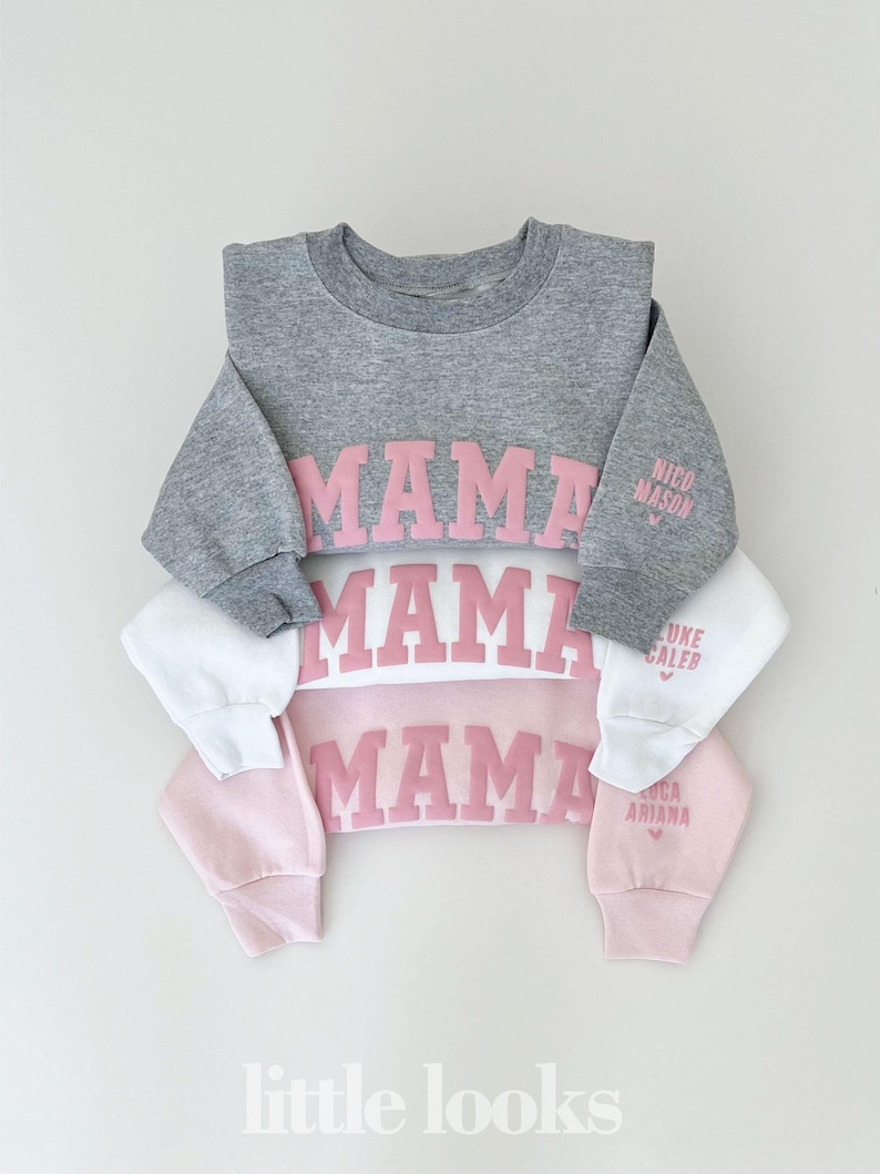 May include: Three gray, white, and pink sweatshirts with the word "MAMA" in pink letters on the front. The sleeves of each sweatshirt have a name and a heart printed on them. The names are "Nico Mason", "Luke Caleb", and "Luca Ariana".