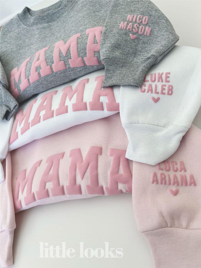 May include: Four pink sweatshirts with the word "MAMA" in pink raised letters. The sleeves of each sweatshirt have a different name and a heart printed on them. The names are "Nico Mason", "Luke Caleb", "Luca", and "Ariana". The text "little looks" is printed on the bottom of the image.