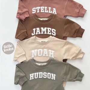 May include: Five long-sleeved baby onesies in different colors with white embroidered names: Olivia, Stella, James, Noah, and Hudson.