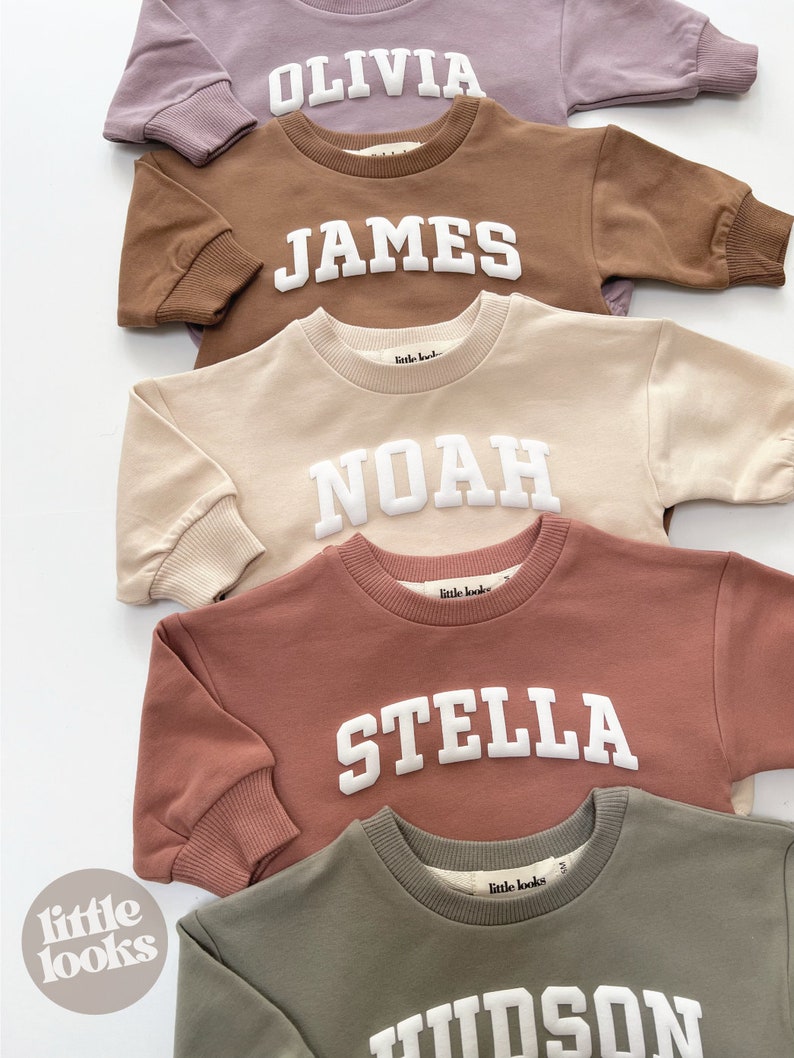 May include: Five personalized sweatshirts in different colors with names in white block letters. The names are Olivia, James, Noah, Stella, and Hudson. The sweatshirts are all from the brand "little looks".
