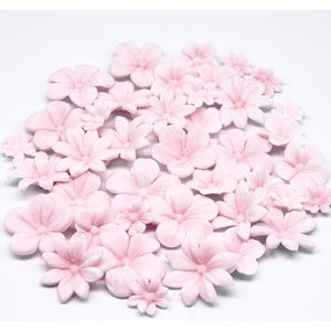 May include: A collection of light pink, artificial flowers of varying sizes, arranged on a white surface. The flowers have multiple petals and a detailed center, creating a delicate and floral aesthetic. Ideal for crafting or decoration.