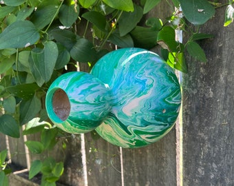 May include: A green and white gourd with a marbled pattern is hanging on a wooden fence. The gourd has a hole in the side.