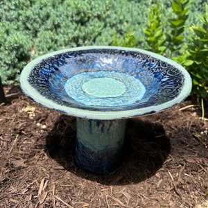 May include: A blue and green ceramic bird bath with a decorative design. The bird bath has a wide, shallow bowl and a tall, cylindrical base.