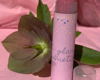 May include: A pink lip balm tube with a pink and white speckled design. The tube has the text "t-glam cosmetics" printed on it. The lip balm is in a clear plastic container.