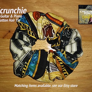 May include: A black and white scrunchie with a guitar and piano design. The scrunchie is made of cotton and has a yellow, blue, and orange pattern. The text "Scrunchie" is written in white letters on a black background. The text "1 Guitar & Piano Cotton Hair Tie" is written in white letters on a black background. The text "CHESTNUT PONY Designs" is written in white letters on a black background. The text "Matching items available, see our Etsy store" is written in white letters on a black background.