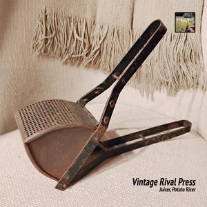 May include: Vintage Rival Press juicer and potato ricer. The kitchen tool is made of metal with a perforated bowl and black handles. The text "Vintage Rival Press" is visible.