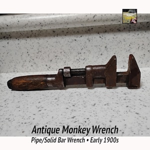 May include: Antique monkey wrench with a wooden handle and adjustable jaws. The wrench is made of metal and shows signs of age and wear. The text on the image reads "Antique Monkey Wrench Pipe/Solid Bar Wrench • Early 1900s."