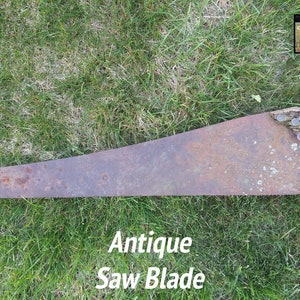May include: An antique saw blade with a weathered, rusty appearance. The blade is long and triangular, with a jagged edge. The handle is made of a piece of wood attached with metal fasteners. The text "Antique Saw Blade" is displayed on the image.