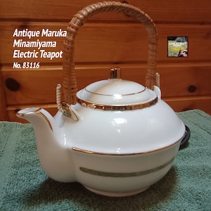 May include: Antique white electric teapot with a woven wicker handle, gold trim, and a gold and white floral design. The teapot is labeled "Antique Maruka Minamiyama Electric Teapot No. 83116".