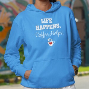 Peut inclure: Un sweat à capuche bleu clair avec un motif blanc qui dit "Life Happens. Coffee Helps." et un petit cœur rouge dans une tasse de café.