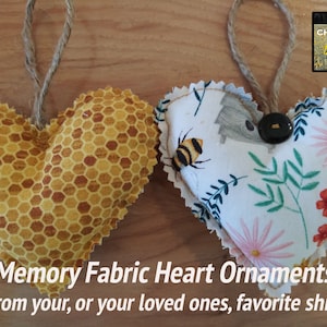 May include: Two fabric heart ornaments, one with a honeycomb pattern and the other with a floral pattern, both with a brown twine hanger. The text "Memory Fabric Heart Ornaments" and "From your, or your loved ones, favorite shirt" is below the ornaments.