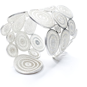 Puede incluir: Un brazalete de plata hecho de círculos y óvalos interconectados, cada uno con un patrón delicado e intrincado.