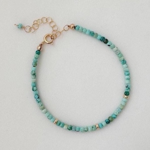 May include: A turquoise beaded bracelet with gold-coloured details. The bracelet is made up of small, round turquoise beads, connected by gold-coloured metal links and a clasp. The adjustable chain allows for a comfortable fit. A simple and elegant piece of jewellery.