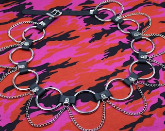 May include: A black leather belt with silver metal rings and chains. The belt is on a pink and red camouflage fabric background.