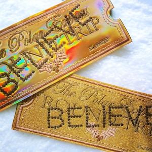 May include: Two gold-coloured, rectangular tickets with decorative edges. The top ticket has iridescent holographic foil and reads "The Polar Express TRIP" in embroidered script. The bottom ticket reads "The Polar Express" in embroidered script.