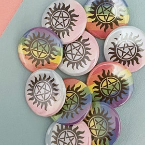 May include: A set of eight round buttons featuring a black pentagram inside a sun symbol on a rainbow background. The buttons are arranged in a circle with the rainbow colours facing outwards.