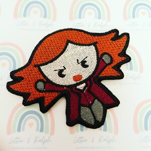 May include: Iron-on patch featuring an embroidered cartoon character with red hair, a red and burgundy outfit, and a serious expression. The character is in a superhero pose with one arm raised.