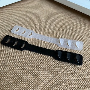 May include: Two face mask extenders, one white and one black. Both extenders have multiple small bumps on the surface and are designed to help keep a face mask from pulling on the ears.