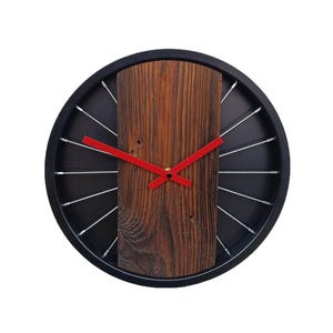 May include: A black and brown clock with red hands. The clock face is made of metal with spokes radiating from the centre. The clock is surrounded by a black frame.