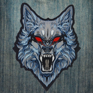 May include: Embroidered patch featuring a detailed wolf head with an open mouth, bared teeth, and glowing red eyes. The wolf's fur is rendered in shades of gray and blue, with a black border. The patch is likely for jackets or bags.