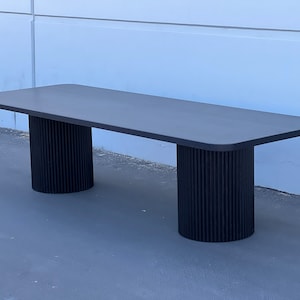 May include: A long, black, rectangular table with rounded edges. The table is supported by two black, fluted, cylindrical legs.