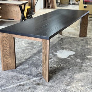 May include: A rectangular wooden table with a black top and light brown legs. The table has a modern design, with the legs positioned at the corners. The wood grain is visible on both the tabletop and the legs.