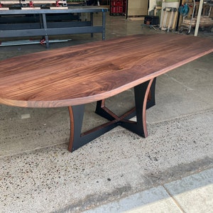 May include: A large oval wooden table with a dark walnut finish and a black metal base. The table has a unique X-shaped base with curved supports.
