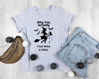 May include: A gray t-shirt with a black silhouette of a witch flying on a broomstick with a black cat. The text on the shirt reads "Why Yes, Actually, I Can Drive A Stick."