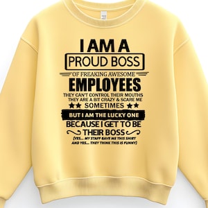 Puede incluir: Una sudadera amarilla clara con el texto "I AM A PROUD BOSS OF FREAKING AWESOME EMPLOYEES" en negro. El texto incluye declaraciones humorísticas sobre los empleados y el jefe. La sudadera tiene cuello redondo y mangas largas.