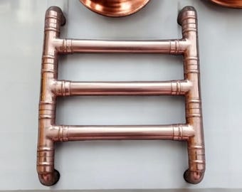 May include: A copper towel rack with three bars. The rack is mounted on a white wall and has a wooden surface below it.