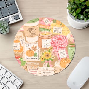May include: A round mouse pad featuring a colorful autumn-themed illustration with pumpkins, a candle, a coffee cup, a plaid scarf, sunflowers, and books. The design includes text such as One More Chapter, Cozy Nights, Soft Lights, and Sweater Weather Reader.
