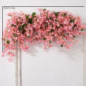 May include: A cascade of pink artificial bougainvillea flowers with green leaves, 1 metre long and 0.5 metres wide. The floral arrangement is displayed against a white background, creating a vibrant and decorative display.