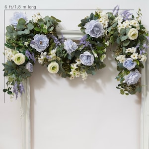 Könnte beinhalten: Eine 1,8 m lange Girlande aus künstlichen Blumen mit blauen und weißen Blüten, grünen Blättern und Lavendelzweigen. Die Girlande ist über einen weißen Rahmen gelegt.