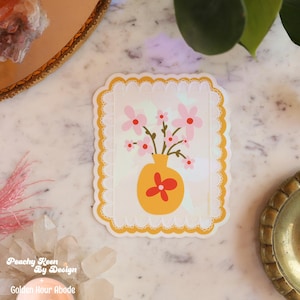Può includere: Un adesivo con un design floreale. L'adesivo presenta un vaso giallo con fiori rosa e un accento floreale rosso. L'adesivo ha uno sfondo bianco con un bordo giallo smerlato. Il testo "Peachy Keen By Design" e "Golden Hour Abode" è in basso.