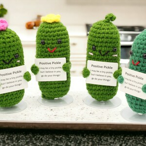 May include: Four green crocheted pickle plushies holding signs that say "Positive Pickle I may be a tiny pickle, but I believe in you, go do your things!"