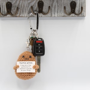 May include: A brown crocheted potato keychain with a white card attached that reads "Positive potato I may be a tiny potato, but I believe in you Go do your thing!"