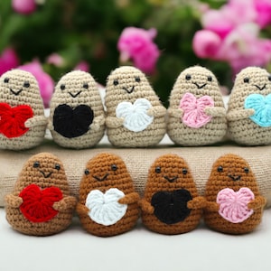 May include: Eight crocheted potato-shaped figures holding different colored hearts. The figures are beige, brown, and tan. The hearts are red, black, white, pink, and blue.