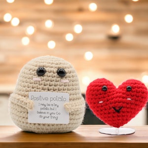 May include: A crocheted potato holding a card that says "Positive potato I may be a tiny potato but I believe in you Go do your thing!"  Next to the potato is a crocheted red heart.