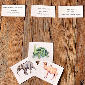 May include: Four cards with animal descriptions and pictures of an elephant, a camel, a tortoise, and a card with the text "I AM BIG. I AM GREY. I HAVE TUSKS AND A TRUNK."