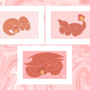 May include: Three rectangular art prints featuring stylised orange lizard-like creatures on a light pink background. Each print depicts a different pose with a small flame element, white speckles, and a small square signature mark in the corner.