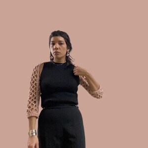 Può includere: Una persona indossa una canotta nera con una spallina in crochet rosa. La persona indossa pantaloni neri e ha i capelli corti e scuri.