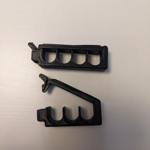 May include: Two black plastic cable organizers with multiple slots for holding cables. The organizers are designed to be mounted on a wall or surface.