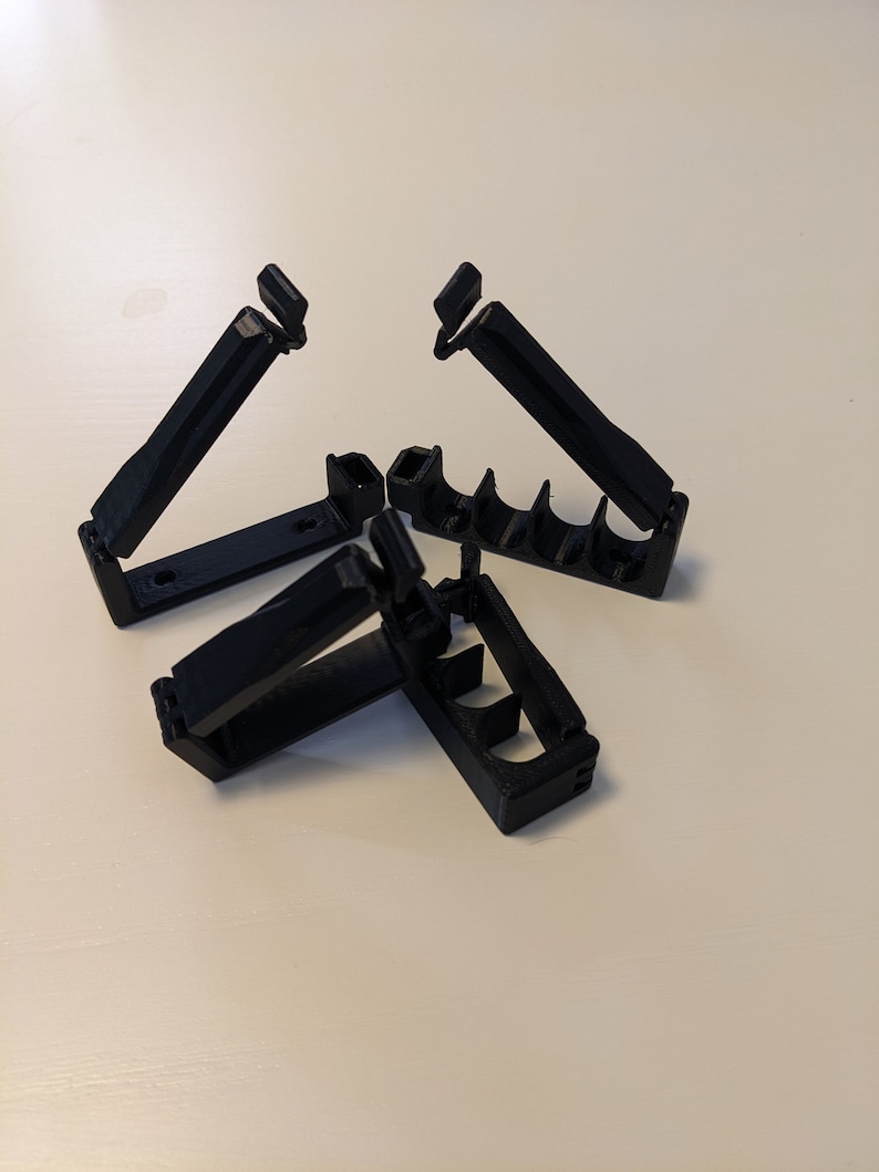 May include: Three black plastic cable clips, designed to hold cables together. The clips are open and ready to be used.