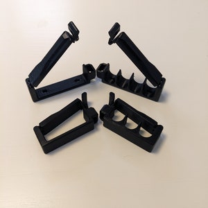 May include: Four black plastic cable clips, two with a single slot and two with three slots, designed to hold and organize cables.