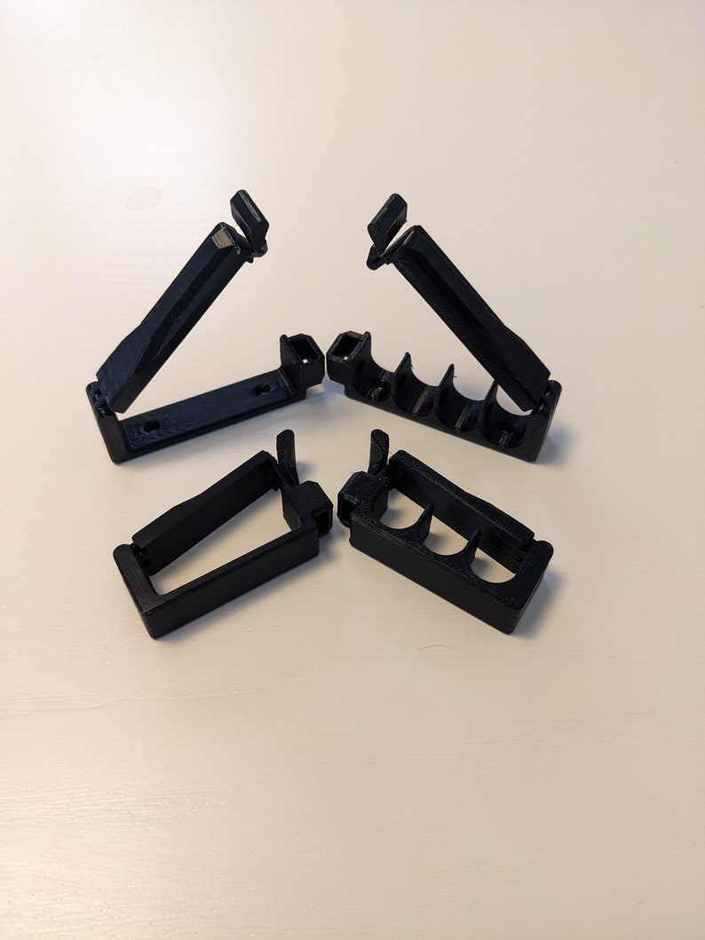 May include: Four black plastic cable clips, two with a single slot and two with three slots, designed to hold and organize cables.