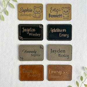 May include: A collection of eight rectangular leather name tags in various shades of brown, black, and gray. Each tag features a name, with some including an engraved animal illustration such as a fox, bear, or bunny. The tags are stitched around the edges.