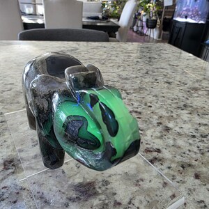 May include: A carved stone elephant figurine featuring a polished surface with deep black and vibrant green marbled patterns. The elephant is positioned on a clear acrylic stand, and the text "I. Michelle Crystals" is visible in the bottom left corner.