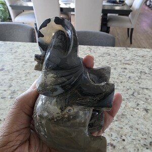 May include: A carved stone elephant figurine featuring a polished surface with swirling patterns in shades of black, gray, and translucent white. The sculpture displays natural banding and mineral inclusions throughout its form. Text reads I. Michelle Crystals.