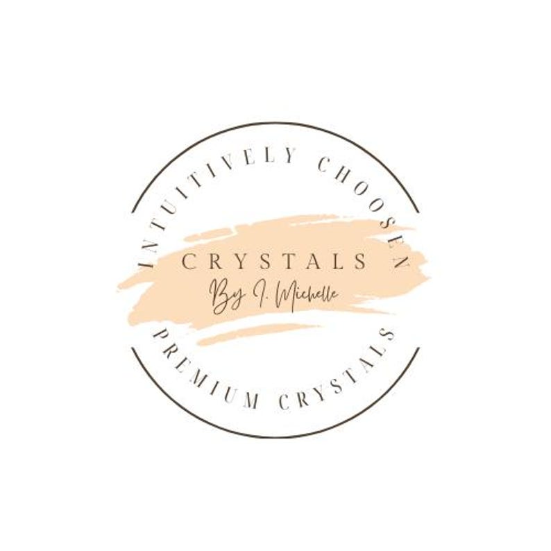 May include: A circular logo featuring a dark brown outline with the text INTUITIVELY CHOSEN and PREMIUM CRYSTALS. In the center, a light peach-colored brushstroke background displays the text CRYSTALS By J. Michelle in dark brown lettering.